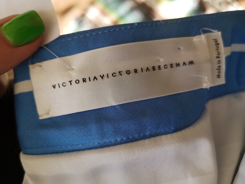 May include: A white label with black text that reads "VICTORIA VICTORIA BECKHAM" and "Made in Portugal". The label is attached to a blue and white striped fabric.