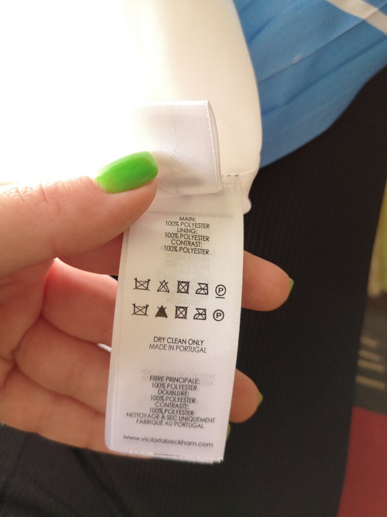 May include: White care label with black text and symbols. The label states "Main: 100% Polyester, Lining: 100% Polyester, Contrast: 100% Polyester". The label also includes instructions for dry cleaning only and states "Made in Portugal".