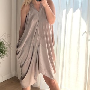 Puede incluir: Vestido sin mangas de color topo con escote en V y dise&ntilde;o asim&eacute;trico drapeado. El vestido tiene un ajuste holgado y relajado y parece estar hecho de una tela suave y sedosa. El vestido llega a la rodilla y es adecuado para ocasiones informales o semiformales.
