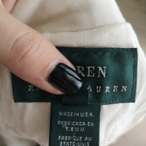 May include: A white garment tag with green trim and the text "Ralph Lauren" in black lettering. The tag also includes the text "Made in U.S.A." "Fabricada en E.E.U.U." and "Fabrique au Etats-Unis".