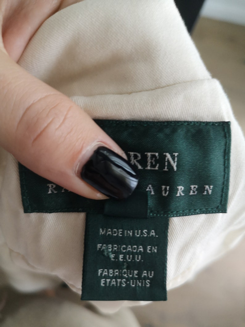 May include: A white garment tag with green trim and the text "Ralph Lauren" in black lettering. The tag also includes the text "Made in U.S.A." "Fabricada en E.E.U.U." and "Fabrique au Etats-Unis".