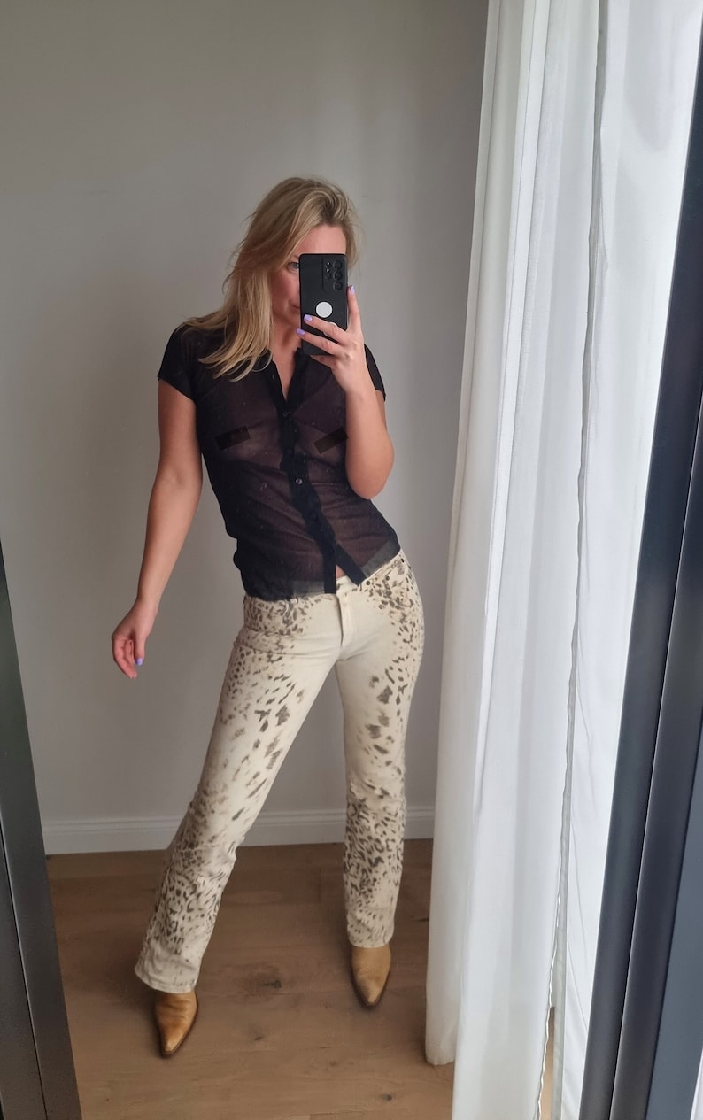 May include: A woman wearing a black sheer button-up shirt with short sleeves and beige pants with a leopard print.