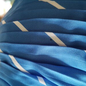 May include: Close-up of a blue and white striped fabric with a pleated texture. The fabric is soft and has a subtle sheen.