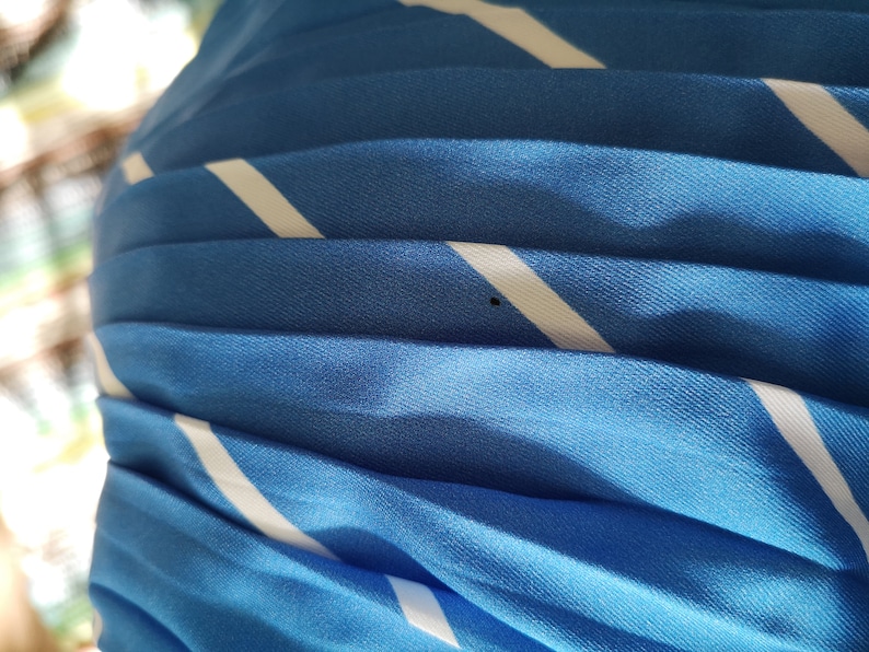 May include: Close-up of a blue and white striped fabric with a pleated texture. The fabric is soft and has a subtle sheen.