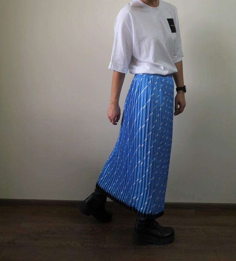 May include: A blue pleated skirt with a white geometric pattern. The skirt is midi length and has a black waistband.
