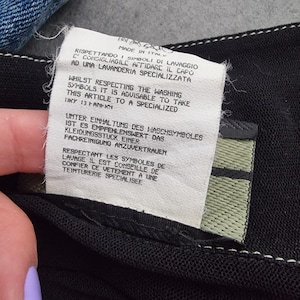 May include: A white tag with black text detailing care instructions for a garment. The tag reads "Rispettando i simboli di lavaggio c'consigliabile affidare il capo ad una lavanderia specializzata" in Italian, "Whilst respecting the washing symbols it is advisable to take this article to a specialized" in English, "Unter Einhaltung des Waschsymboles ist es empfehlenswert das Kleidungsst&uuml;ck einer Fachreinigung anzuvertrauen" in German, and "Respectant les symboles de lavage il est conseill&eacute; de confier ce v&ecirc;tement &agrave; une teinturerie sp&eacute;cialis&eacute;e" in French.