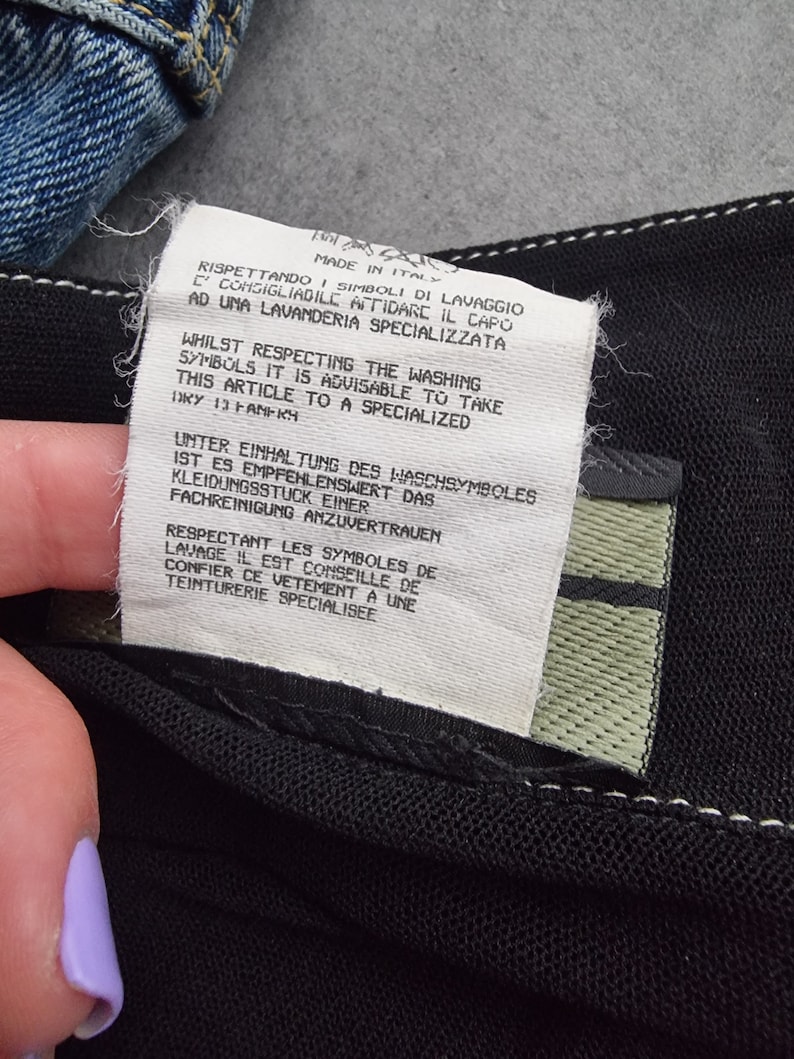 May include: A white tag with black text detailing care instructions for a garment. The tag reads "Rispettando i simboli di lavaggio c'consigliabile affidare il capo ad una lavanderia specializzata" in Italian, "Whilst respecting the washing symbols it is advisable to take this article to a specialized" in English, "Unter Einhaltung des Waschsymboles ist es empfehlenswert das Kleidungsst&uuml;ck einer Fachreinigung anzuvertrauen" in German, and "Respectant les symboles de lavage il est conseill&eacute; de confier ce v&ecirc;tement &agrave; une teinturerie sp&eacute;cialis&eacute;e" in French.
