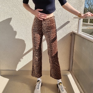 Puede incluir: Pantal&oacute;n de pierna ancha con estampado de leopardo marr&oacute;n y beige. El pantal&oacute;n se lleva con zapatillas blancas y calcetines blancos.