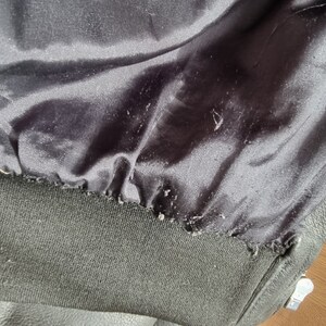 Op de afbeelding: Close-up van de binnenkant van een zwart leren jack, met de zwarte voering en een zwarte geribbelde brede boord.