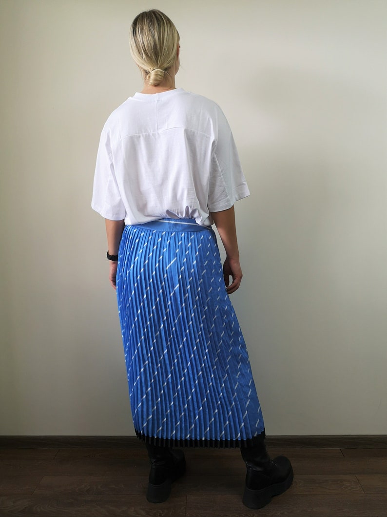 May include: A blue pleated skirt with a white geometric pattern. The skirt is midi length and has a black waistband.