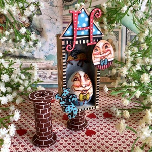 May include: A whimsical wooden house with a blue and white roof, a large letter "H" on the front, and a small egg-shaped face with a bow tie peeking out of a window. The house is sitting on a brick base and is surrounded by white flowers.