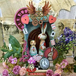 May include: A whimsical, handmade wooden box featuring a white rabbit, a girl in a blue dress, and a clock face. The box is decorated with playing cards, hearts, and gears. The text "MR. W. RABBIT" is on the bottom of the box.