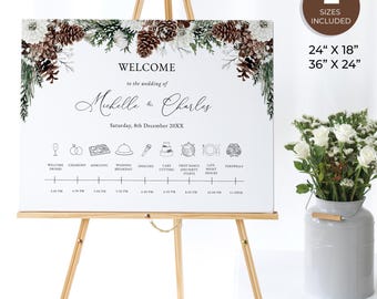 May include: A white wedding welcome sign with a wintery pine cone and greenery design. The sign includes the names Michelle and Charles, the date Saturday, 8th December 20XX, and a wedding day timeline with icons and times.