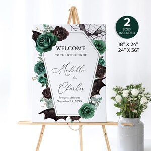 May include: A white wedding welcome sign on an easel, featuring a coffin-shaped design with the text "Welcome to the Wedding of Michelle & Charles." The sign is decorated with green and burgundy roses, bats, and a spiderweb. Includes 18" x 24" and 24" x 36" sizes.