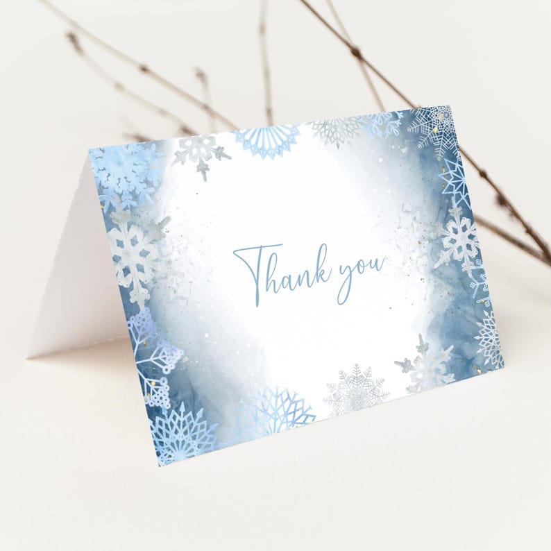 May include: A folded greeting card with a winter theme. The card features a watercolor design with blue and white snowflakes and the words "Thank you" in a script font. The card is on a white background.