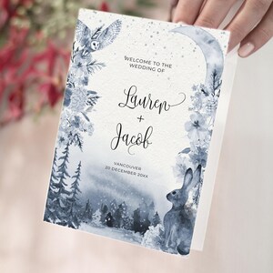 以下が含まれることがあります： 水彩デザインの折り畳まれた結婚式の招待状。「Lauren + Jacob」の名前と結婚式の日付が記載されています。デザインには、フクロウ、ウサギ、花、三日月が青と白の色合いで描かれています。