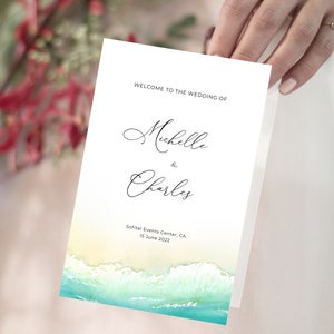 May include: Wedding program with a beach theme. The program features a watercolor background of ocean waves and sand. The text reads "Welcome to the Wedding of Michelle & Charles, Sofitel Events Center, CA, 15 June 2022."