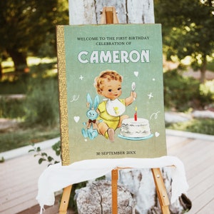 May include: A green and yellow birthday sign with a vintage illustration of a baby boy holding a spoon and a bunny. The sign says "Welcome to the first birthday celebration of CAMERON 30 September 20XX".
