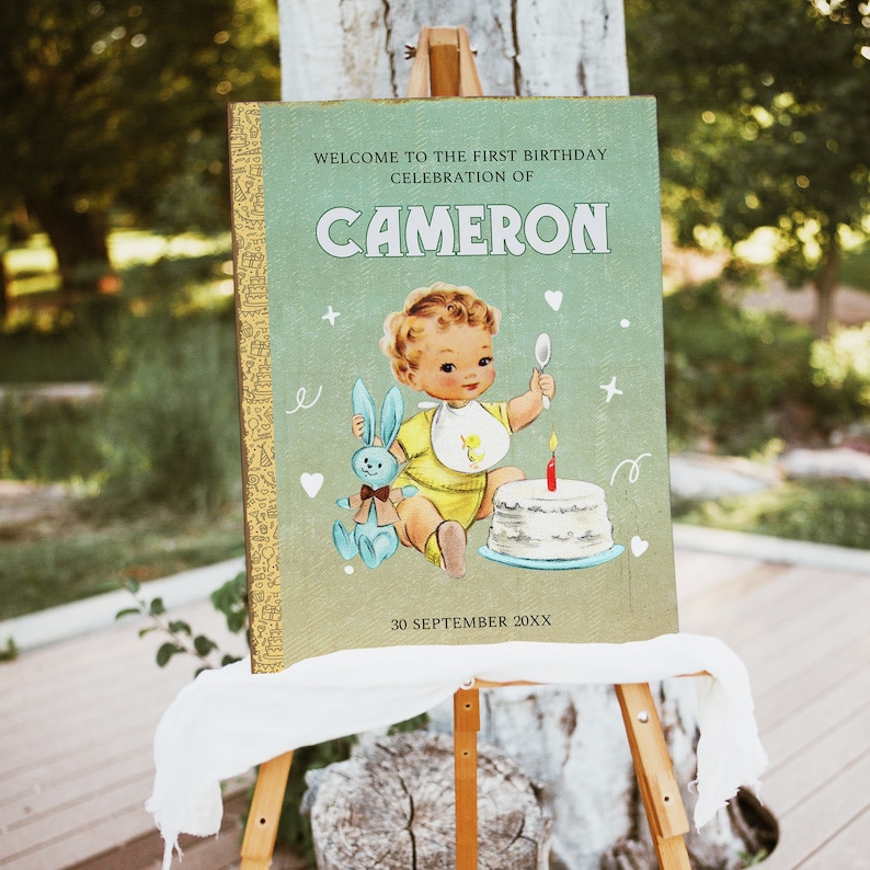 May include: A green and yellow birthday sign with a vintage illustration of a baby boy holding a spoon and a bunny. The sign says "Welcome to the first birthday celebration of CAMERON 30 September 20XX".