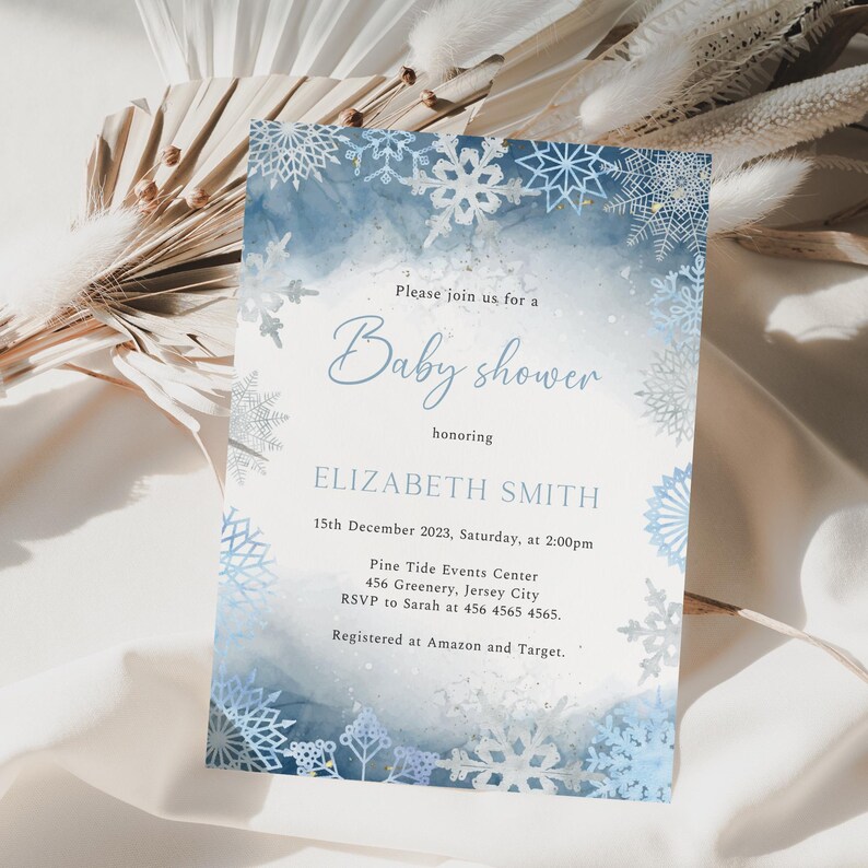 May include: A baby shower invitation with a winter theme. The invitation features a watercolor background in shades of blue and white, with snowflake accents. The text reads "Baby shower" and includes the honoree's name, date, time, and location.