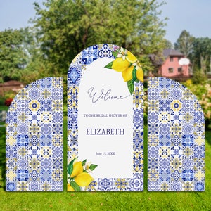 Puede incluir: Tres letreros de bienvenida en forma de arco azul y amarillo con un patrón de azulejos. El letrero del centro tiene el texto "Bienvenido al baby shower de Elizabeth el 15 de junio de 20XX".