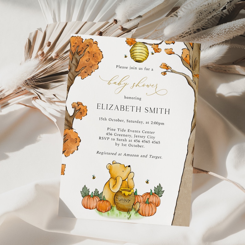 May include: Baby shower invitation featuring a watercolor illustration of Winnie the Pooh with pumpkins and a honey pot. The invitation includes event details, such as the date, time, and location, with the text "baby shower" in elegant script.