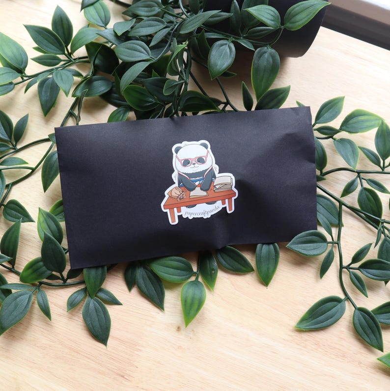 May include: A black and white panda wearing sunglasses and a blue shirt sits at a desk with a stack of papers and a cup of coffee. The sticker says "papercraftpanda".