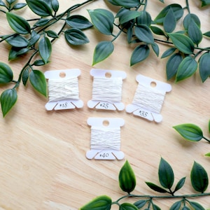 May include: Four white spools of thread on white plastic bobbins with the numbers 18, 25, 35, and 40 printed on them.