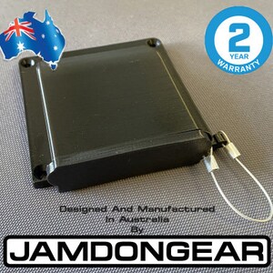 Könnte beinhalten: Eine schwarze rechteckige Box mit einem 2-Jahres-Garantieaufkleber. Die Box hat ein silbernes Kabel daran befestigt. Der Text "Designed And Manufactured In Australia By JAMDONGEAR" ist unter der Box aufgedruckt.