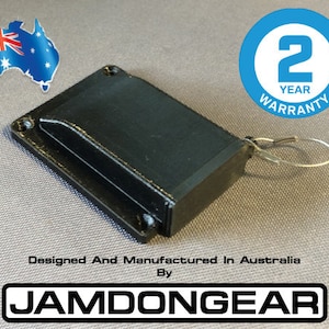 May include: Black electronic device with a small, rectangular opening. The device is attached to a silver wire loop. The text "Designed And Manufactured In Australia By JAMDONGEAR" is printed below the device.