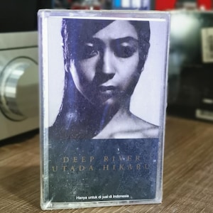 May include: A cassette tape featuring a black and white portrait of a woman. The album title "DEEP RIVER" and artist "UTADA HIKARU" are printed on the cover. The text "Hanya untuk di jual di Indonesia" is also visible.