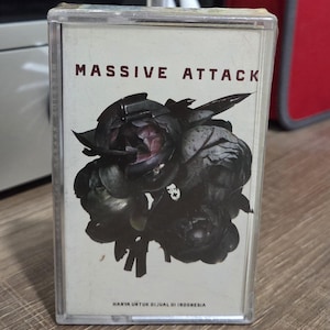 May include: A cassette tape with the text "MASSIVE ATTACK" in maroon. The cover features a dark floral design. The text "HANYA UNTUK DIJUAL DI INDONESIA" is also visible. The cassette is in a clear plastic case.