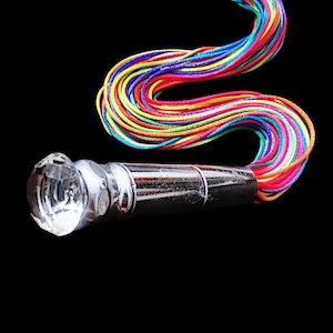May include: A decorative bottle stopper with a faceted crystal top and a shiny silver metal body. A colorful rainbow of cords extends from the stopper against a black background. The cords are a mix of red, orange, yellow, green, blue, and purple.