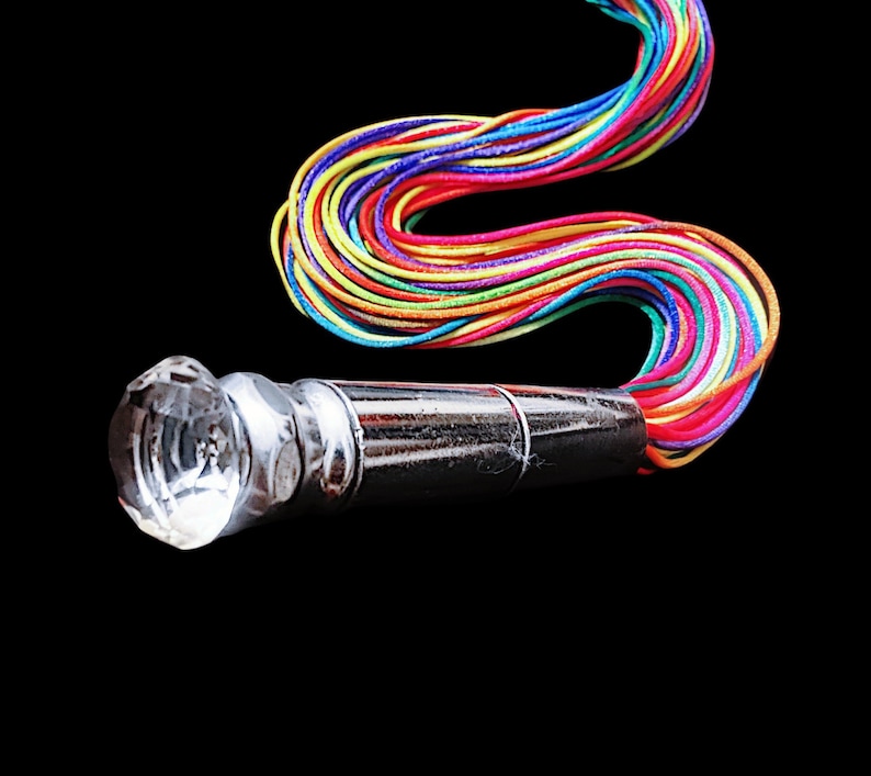 May include: A decorative bottle stopper with a faceted crystal top and a shiny silver metal body. A colorful rainbow of cords extends from the stopper against a black background. The cords are a mix of red, orange, yellow, green, blue, and purple.