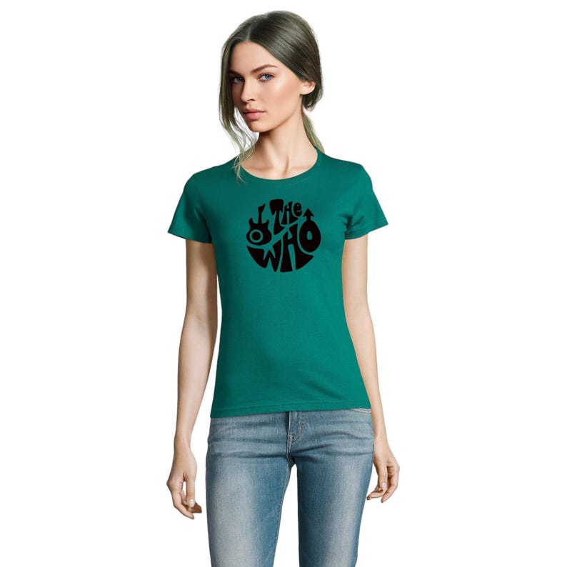May include: Teal t-shirt with a black circular design featuring the text "The Who" and musical instrument silhouettes. The shirt is made of a soft material and has short sleeves.