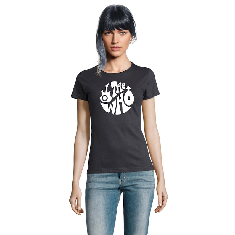 May include: A dark grey t-shirt with a white circular design featuring the band name "The Who" and musical instrument graphics. The shirt is short-sleeved and worn with blue jeans.