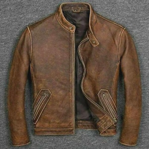 May include: A brown leather jacket with a stand-up collar and a zipper closure. The jacket has two zippered pockets and a distressed finish, giving it a vintage look. The jacket is a classic style, suitable for various occasions.