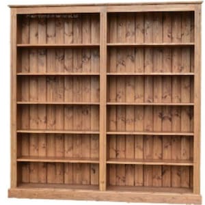 May include: A large wooden bookcase with a natural finish. The bookcase is divided into two sections, each with multiple shelves for storage. The wood grain is visible, giving it a rustic appearance. The shelves are evenly spaced.
