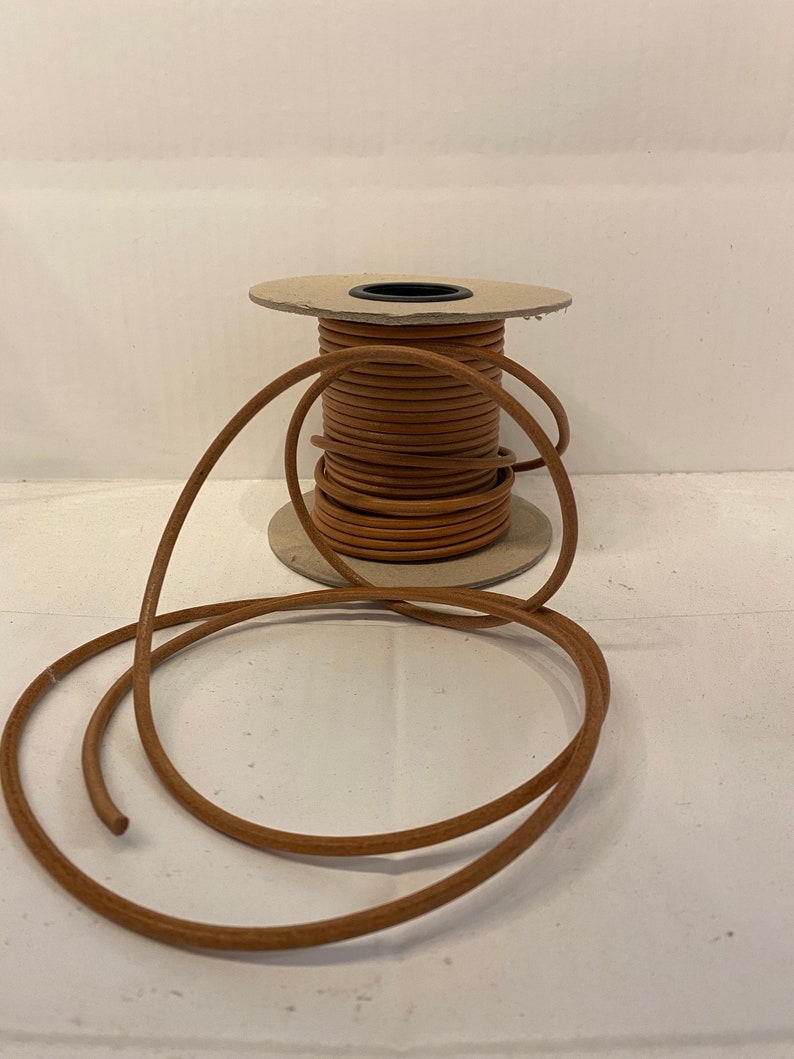 May include: A spool of brown leather cord, wound around a cardboard spool. The cord is about 3/16 inch thick and is ready to be used for crafting projects.