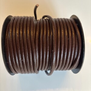 May include: A spool of brown leather cord. The cord is wound tightly around a black plastic spool.