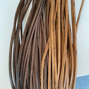 Puede incluir: Dos haces de cordón de cuero marrón, uno es marrón oscuro y el otro es marrón claro.