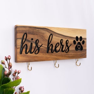 Op de afbeelding: Houten sleutelhanger met de woorden "his hers" en een pootprint met een hart in het midden. Er zijn drie haken om sleutels aan te hangen.