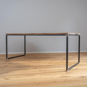 Könnte beinhalten: Ein rechteckiger Holztisch mit einem schwarzen Metallgestell. Der Tisch steht auf einem Holzboden.