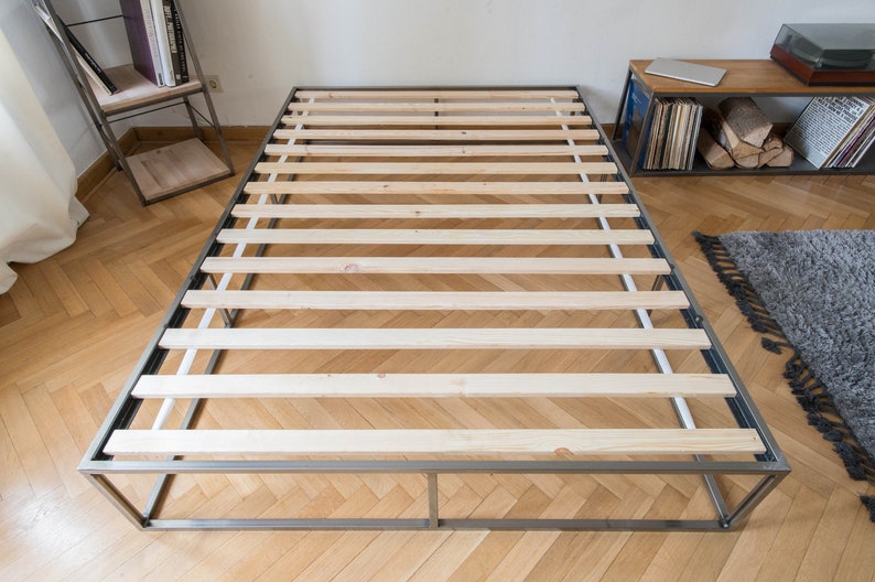 May include: A metal bed frame with a slatted wooden base. The frame is silver and the slats are light wood.