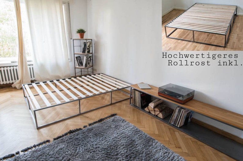 May include: A metal bed frame with a slatted base. The frame is made of black metal and has a simple, modern design. The bed frame is sitting on a wooden floor with a gray rug in front of it.
