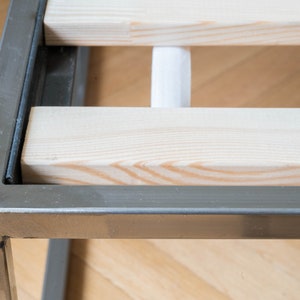 May include: Close-up of a metal bed frame with wooden slats. The frame is silver and the slats are light wood.