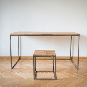 Könnte beinhalten: Ein Holzschreibtisch mit einem Metallrahmen und einem passenden Holzhocker mit einem Metallrahmen. Der Schreibtisch und der Hocker stehen beide auf einem hellen Holzboden.