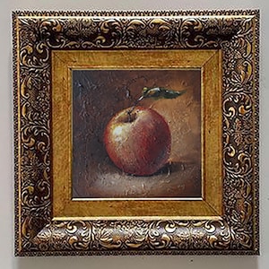 Puede incluir: Pintura al óleo de una manzana roja con una hoja verde, sobre un fondo marrón oscuro. La obra de arte está enmarcada en un marco dorado con detalles ornamentados, lo que añade un toque clásico a la composición de naturaleza muerta.