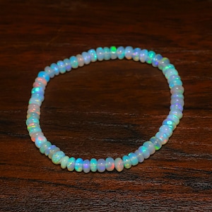 Peut inclure: Un bracelet délicat composé de petites perles d'opale iridescentes. Les perles affichent une gamme de couleurs, dont le blanc, le bleu, le vert et le rose, créant un effet chatoyant. Le bracelet est assemblé en cercle complet.
