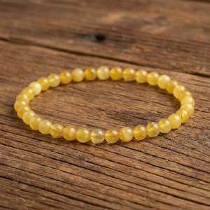 Könnte beinhalten: Ein kreisförmiges Armband, das aus zahlreichen kleinen, glatten, durchscheinenden gelben Perlen besteht. Die Perlen sind in Größe und Form einheitlich und zu einer durchgehenden Schlaufe aufgereiht, die einen gleichmäßigen goldgelben Farbton aufweist.